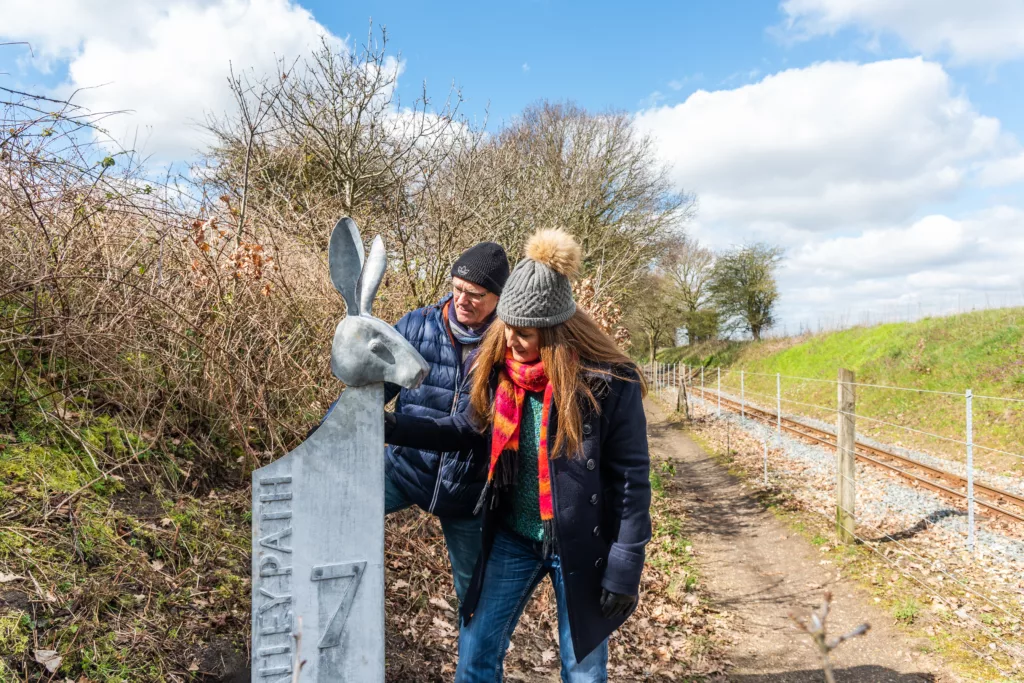 Two people looking at a carved hare head on a waymarker post with text reading "Bure Valley Path 7"