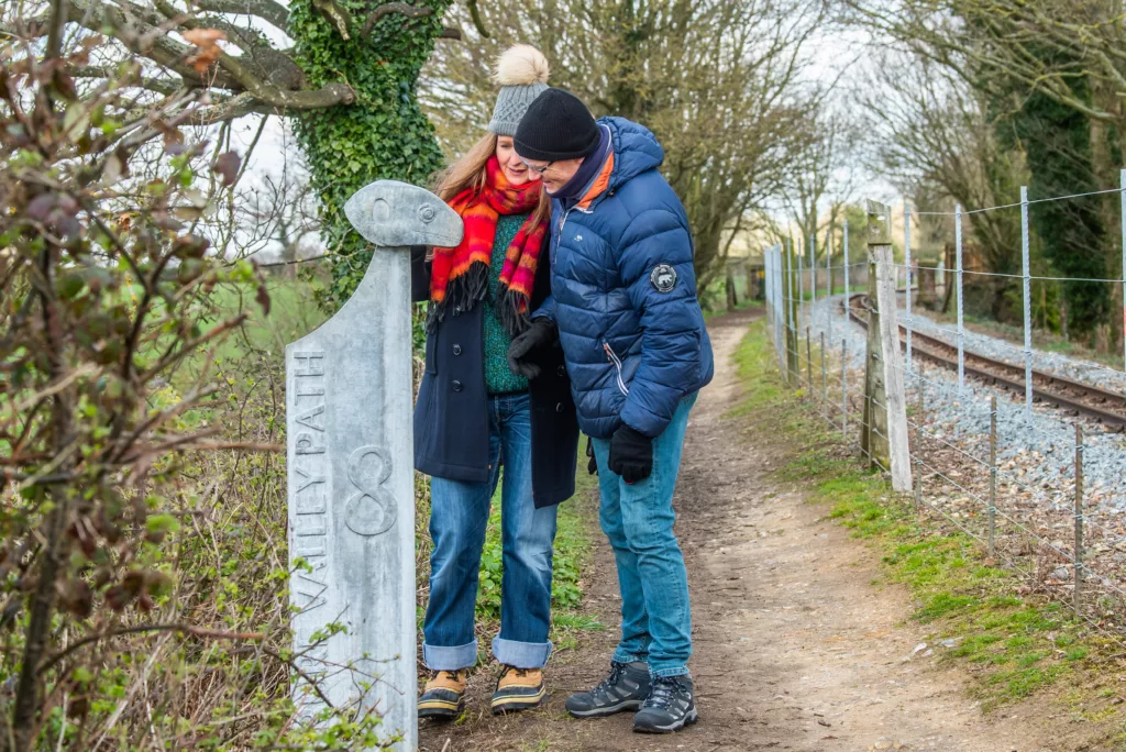 Two people looking at a carved lizard head on a waymarker post with text reading "Bure Valley Path 8"