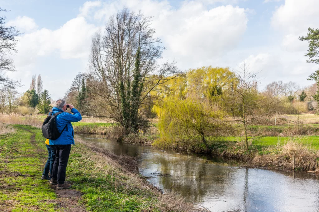 A man with binoculars standing near a river