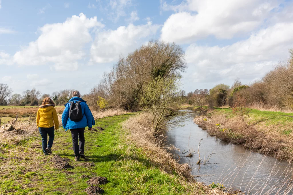 Two people walking on the left side of the riverbank