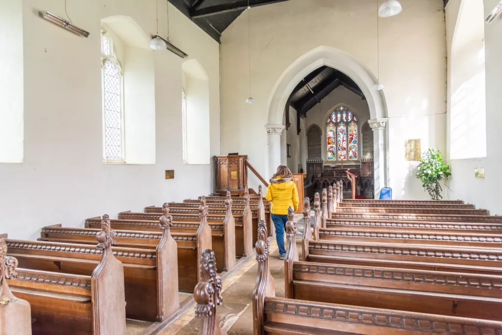 A woman standing between the two rows of pews in All Saints Church, Ashwicken