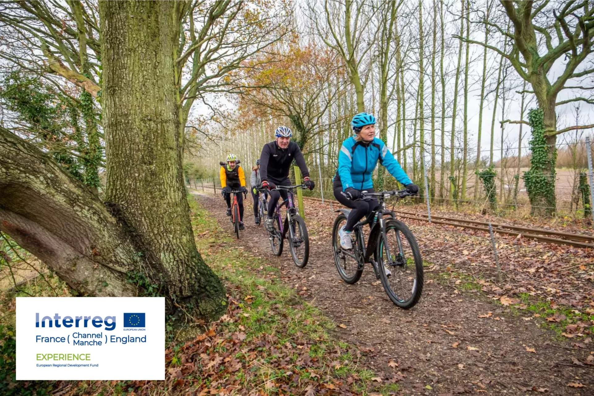 Four people cycling on a wooded trail next to the rail track