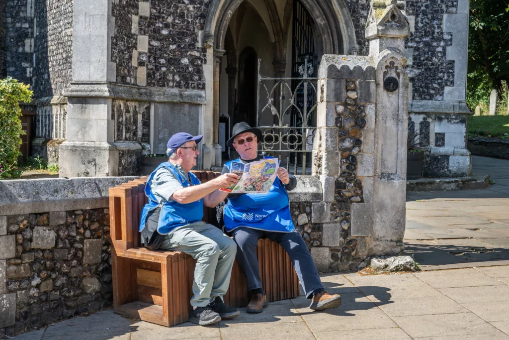 Two people sitting on a bench reading a city map in front of St Stephen's Church, Norwich