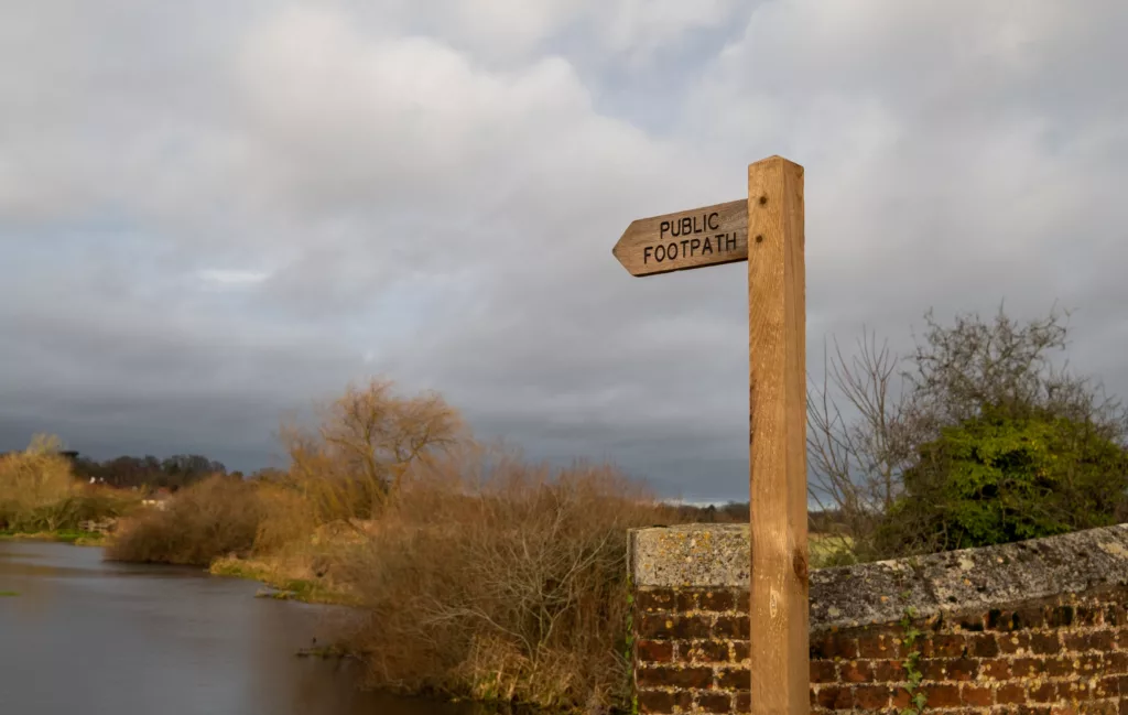 Wooden public footpath sign indicating public access along the bank of the River Bure in the Norfolk village of Buxton.