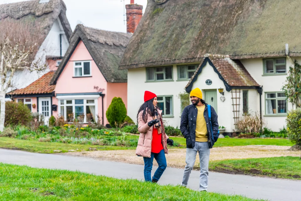 A man and a woman walking past thatched roof houses in Pulham Market